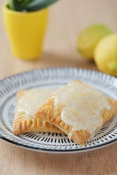 two lemon pastries on a plate next to some lemons and a potted plant