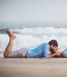 a man and woman laying on the beach kissing