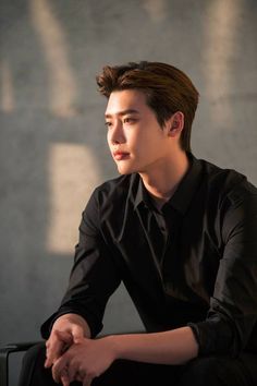 a young man sitting on top of a chair next to a cement wall and looking off into the distance