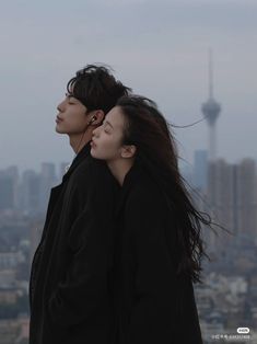 two people standing next to each other in front of a cityscape with the sky tower in the background