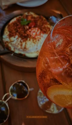 an orange drink and some food on a wooden table with silverware, glasses and napkins