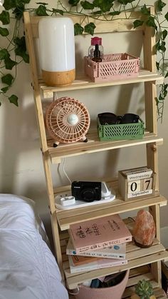 a wooden shelf with books, plants and other items on it next to a bed