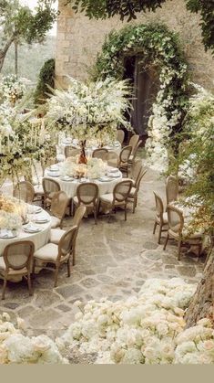 an outdoor dining area with tables, chairs and flowers on the table is surrounded by greenery