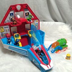 a toy boat with toys in it sitting on a white furnishing area next to a red and blue house