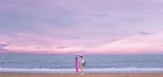 a woman standing on the beach with an umbrella in her hand and looking out at the ocean