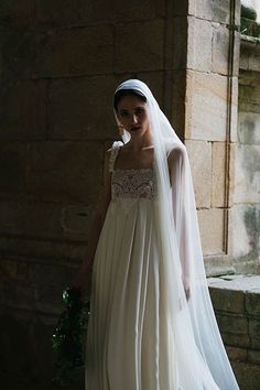 a woman in a white wedding dress standing next to a brick wall wearing a veil