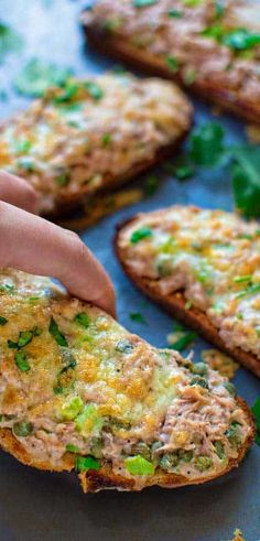 a person reaching for some food on top of a pan covered in green vegetables and bread