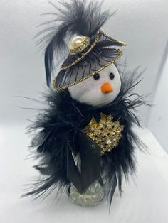 a small glass vase with a snowman decoration on it's head and feathers