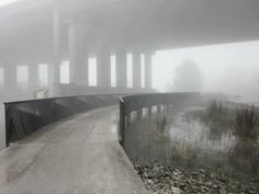 a foggy bridge over a body of water with rocks and grass on the side