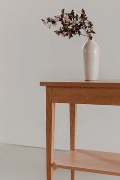 a wooden table with a white vase on it and flowers sitting on top of it