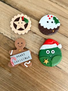 four decorated christmas cookies sitting on top of a wooden table next to a sign that says merry christmas