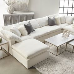 a large white sectional couch with pillows on it's back and side tables in the middle