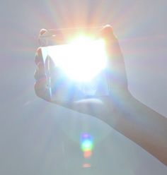 someone holding up their cell phone with the sun shining through it and lens flares in the background