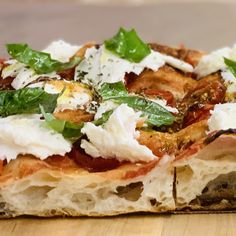 a close up of a slice of pizza with cheese and herbs on top, sitting on a wooden surface