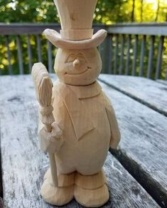 a wooden carving of a snowman holding a cane and wearing a top hat, standing on a picnic table