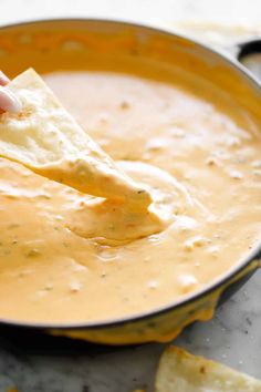 a person dipping tortilla chips into a pot of quesadilla soup