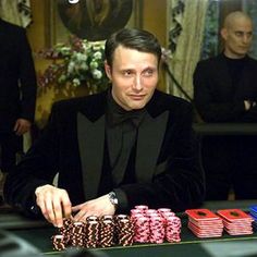 a man in a tuxedo sitting at a table with stacks of poker chips