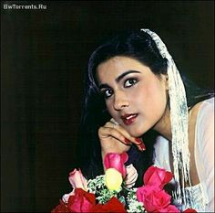 a woman with long black hair wearing a white dress and holding flowers in her hand