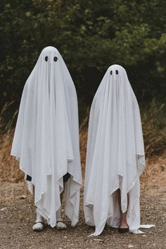 two people dressed in white ghost costumes standing next to each other on a dirt road