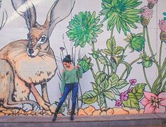 a woman is standing in front of a wall with flowers and a rabbit painted on it