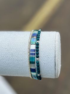 a stack of bracelets sitting on top of a white napkin holder with a blue and green beaded bracelet