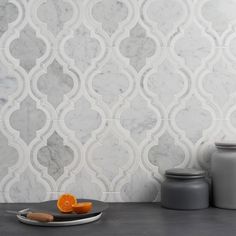 a plate with an orange on it next to some jars and a knife in front of a marble wall