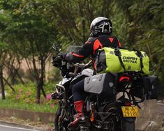 a man riding on the back of a motorcycle down a street next to a lush green forest