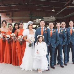 a group of people standing next to each other in front of a brick building wearing orange dresses