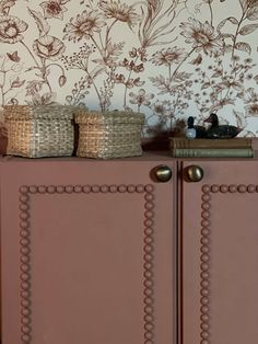 a brown cabinet with baskets on top of it next to a wallpapered wall