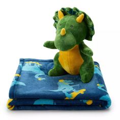 a green stuffed animal sitting on top of a blue and yellow blanket that is folded up