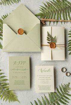 the wedding stationery is laid out with greenery