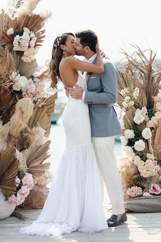 a bride and groom kissing in front of an outdoor wedding arch with flowers on it