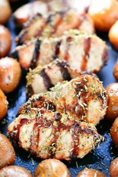 grilled meats and potatoes on a grill with herbs sprinkled on them