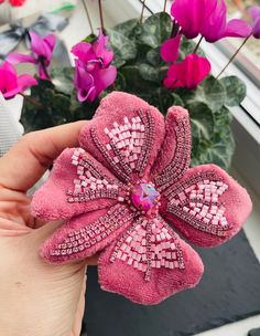 a hand holding a small pink flower with sequins on it's petals