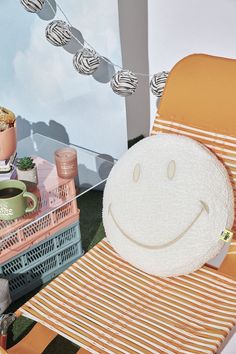 a smiley face pillow sitting on top of a chair next to a table with cups