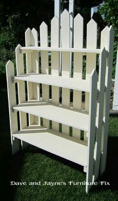 a white book shelf sitting on top of grass next to a fence and trees in the background