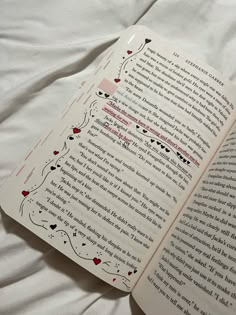 an open book sitting on top of a bed next to a white sheet with red writing