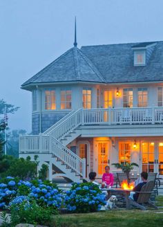 a large white house sitting on top of a lush green hillside next to a fire pit