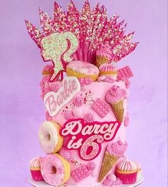 a pink birthday cake decorated with donuts and cupcakes