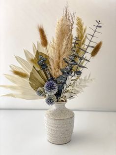 a white vase filled with lots of different types of flowers and plants on top of a table