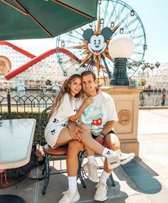 a man and woman sitting on a bench in front of a ferris wheel at an amusement park