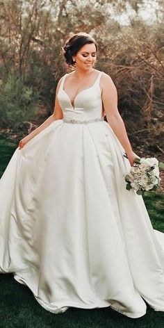 a woman in a wedding dress is walking through the grass