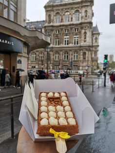 a person holding up a piece of cake in front of a building on the street