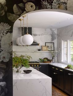 a kitchen with black cabinets and white marble counter tops, an arched doorway leading to the dining room