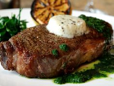 a piece of steak on a white plate with parsley garnish and butter