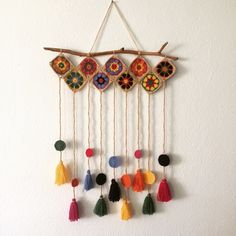 a wall hanging with different colored tassels on it's sides and a wooden stick in the middle