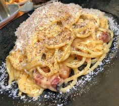 a black plate topped with pasta covered in cheese