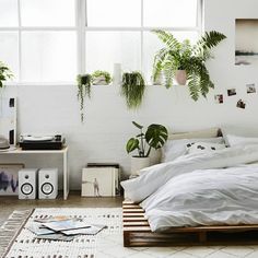 a bed with white sheets and pillows in a room filled with potted plants on the wall