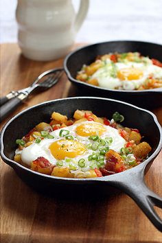 two skillets filled with eggs and vegetables on top of a wooden table