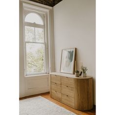 a wooden dresser sitting in front of a window next to a white rug on top of a hard wood floor